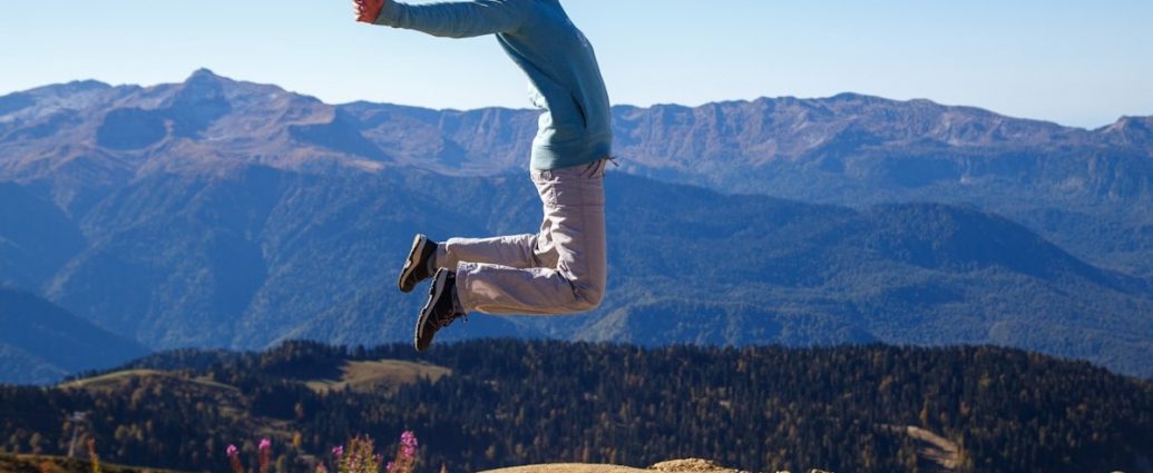 A young woman jumps with outstretched arms against a stunning mountain backdrop, embodying freedom and adventure