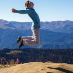 A young woman jumps with outstretched arms against a stunning mountain backdrop, embodying freedom and adventure