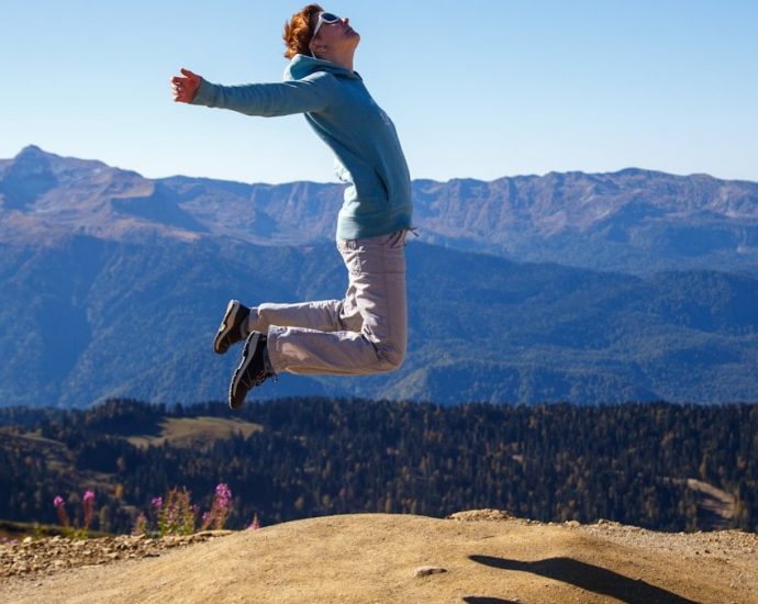 A young woman jumps with outstretched arms against a stunning mountain backdrop, embodying freedom and adventure